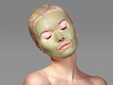 Beautiful Woman Applying Green Facial Mask. Beauty Treatments. Close-up Portrait of Spa Girl Apply Clay Facial mask on grey backgroundの写真素材