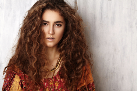 Beautiful young woman with long curly hairstyle, fashion jewelry with long brunette hair. Sexy girl in vogue style. Pretty arabian beauty portrait of female face. Indian style clothes, long dressの写真素材