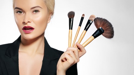 Beauty Treatment. Girl with Makeup Brushes. Fashion Make-up for Sexy Woman. Makeover. Make-up Artist Applying Visage on white backgroundの写真素材