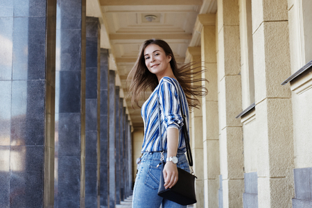 Happy Woman. Street Style Outdoors Portrait of Beautiful Girl. Young Woman Smiling. She wearing Print Shirt, Blue Jeans and Black Bag. Happy Lifestyle shootの写真素材