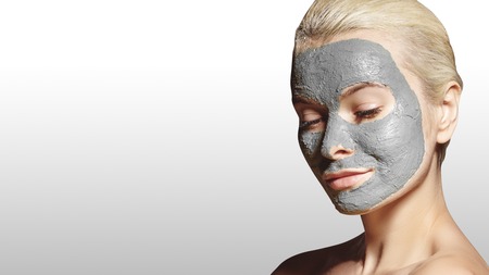 Beautiful Woman Applying White Facial Mask. Beauty Treatments. Close-up Portrait of Spa Girl Apply Clay Facial mask on grey background.の写真素材