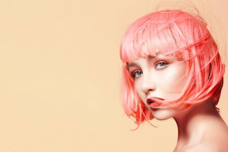 Young model in pink wig. Beautiful model with fashion makeup. Bright spring look. Sexy hair color, medium hairstyle on orange backgroundの写真素材