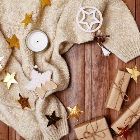 Cozy Winter Composition. Hygge Style. Christmas Gifts, Rustic Decorations, Gold Stars Tinsel and Warm Knitted Sweater on Wood Background. Flat Lay, Top Viewの写真素材