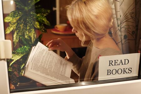 Education and rest at home. Be Healthy, Stay Home. Blond woman reads book. Self isolating while quarantine conceptの写真素材