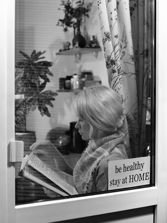Education and rest at home. Be Healthy, Stay Home. Blond woman reads book. Self isolating while quarantine conceptの写真素材