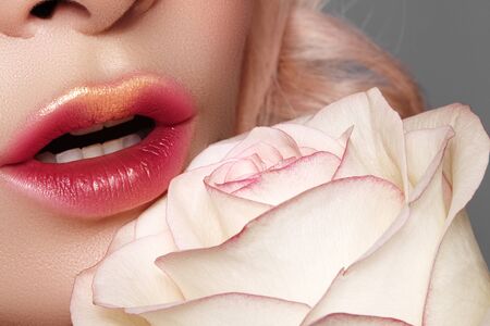 Close-up macro of beautiful female lips with bright kissed makeup. Sexy red tint lip make-up with gold glitter. Beautiful visage with white rose flowerの写真素材