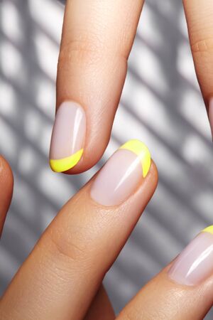 Hands with bright yellow french manicure on geometric background. Nails art design. Close-up of female hands with trendy neon nails on silver striped print backgroundの写真素材
