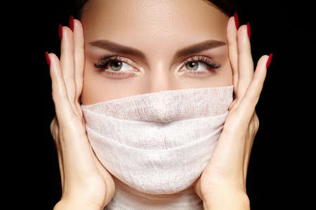 Beautiful woman with bandage mask on face. Fashion eye make-up, long eyelashes and perfect shade eyebrows. Beauty plastic surgery or protection hygiene in viral covid-19 pandemicの写真素材
