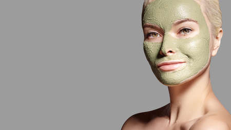 Beautiful Woman Applying Green Facial Mask. Beauty Treatments. Close-up Portrait of Spa Girl Apply Clay Facial mask on grey background.の写真素材
