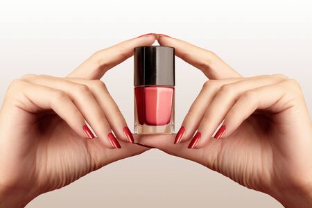 Manicured nails with red nail polish. Manicure with bright nail polish. Fashion manicure. Shiny lacquer in bottle. Hands hold bottle of gel polishの写真素材