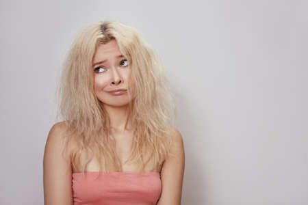 Bad hair day. Beautiful woman with messed up hair. Unhappy grimacing face. Blond bleaching hairstyle with problem brittle hairの写真素材