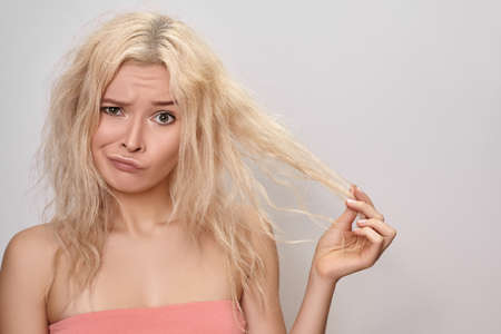 Bad hair day. Beautiful woman with messed up hair. Unhappy grimacing face. Blond bleaching hairstyle with problem brittle hairの写真素材