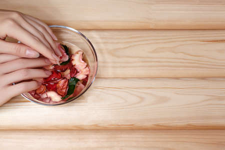Natural Manicure, Hand Care. Soaking Finger Nails in Bath with Herbal Oil and Floral on White Wooden Table. Copy Spaceの写真素材