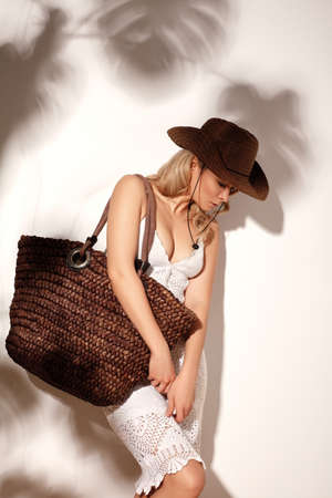 Beautiful Blonde Young Woman Wearing White Crochet Dress and Bown Cowboy Hat under Shade of Foliage. Boho Country Styleの写真素材