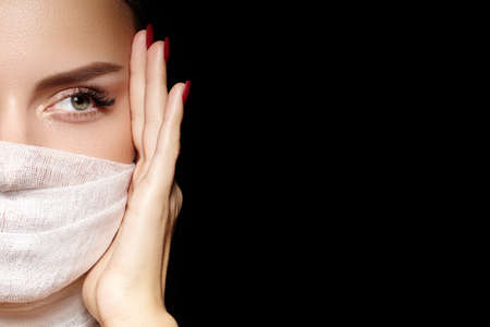 Beautiful woman with bandage mask on face. Fashion eye make-up. Beauty surgery or protection hygiene in virus pandemicの写真素材