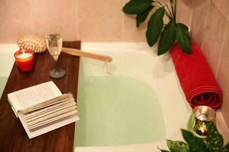 Bath with flower petals. Book, candles and glass of wine on a wood tray. Organic Spa Relaxation in comfort cozy bathroomの写真素材
