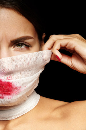 Portrait of woman in bandage mask with red lipstick. Conceptual artistic look for Halloween makeup, Mummy style, plastic surgery clinicの写真素材