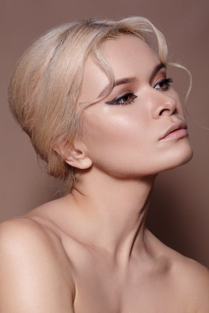 Beautiful sexy model with retro style make-up, clean skin, blond hair bun on beige background. Elegant woman model in femininity pose with fashion make-up, hairstyleの写真素材