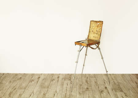 wooden box for drawing and storage of paints, retro artist easel on the floor against a white wall backgroundの写真素材
