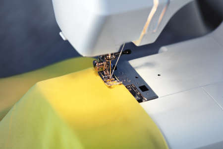 white modern sewing machine close up, yellow backlit synthetic fabric, white thread needle and presser footの写真素材