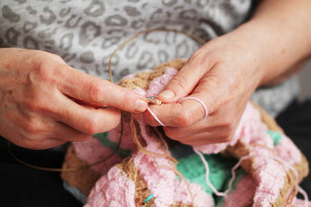 the age hands of a woman with knitting needles knit a product, grandmother's hobby clothes are made...