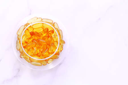 Dietary supplement omega capsules in a round glass vase, yellow transparent vitamins on a marble...