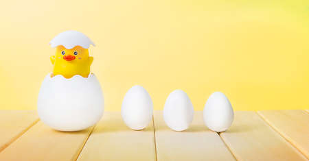 A chick hatches from an egg and three white eggs on a yellow backgroundの写真素材
