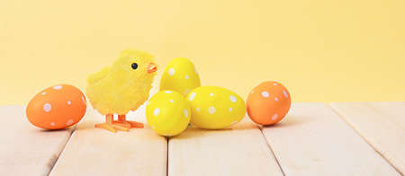 Yellow chicken toy with easter eggs on a wooden backgroundの写真素材