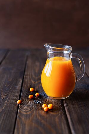 Sea buckthorn juice in a jug and berries on a dark wooden background.の写真素材