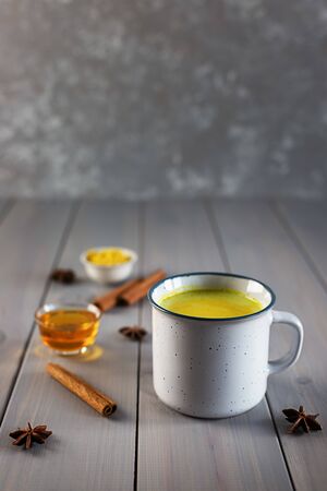 Golden milk in a mug and ingredients for its preparation on a gray wooden background.の写真素材