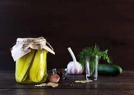 Pickled fermented cucumbers in a glass jar. Pickles with garlic, pepper and dill on a dark brown wooden background.の写真素材