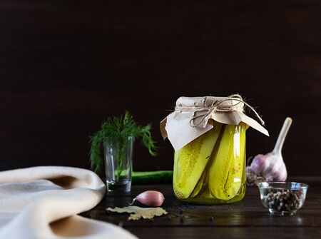 Pickled fermented cucumbers in a glass jar. Pickles with garlic, pepper and dill on a dark brown wooden background.の写真素材