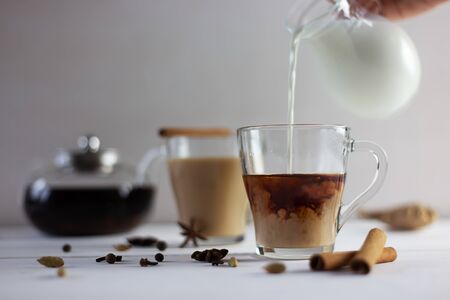 Flavoured masala Indian tea made by brewing black tea with milk, aromatic spices and herbs on white wooden background. Front view.の写真素材
