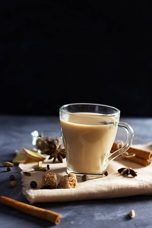 Flavoured masala Indian tea made by brewing black tea with milk, aromatic spices and herbs on grey wooden background. Front view.の写真素材
