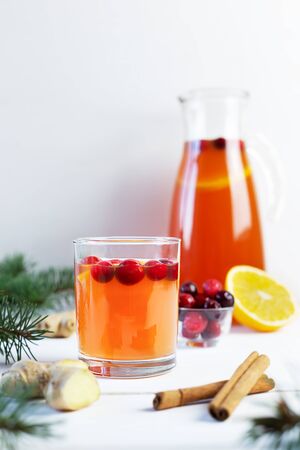 Orange and cranberry non-alcoholic punch with orange slices, cranberries, ginger root and cinnamon on a white wooden table. Hot drinks for winter and Christmas. Front view.の写真素材