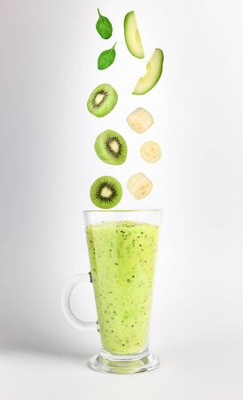 Green smoothie and falling isolated fruits and greens for its preparation: avocado, banana, kiwi and spinach on a neutral pastel gray background. Flying food. Vertical orientation. Space for text.の写真素材