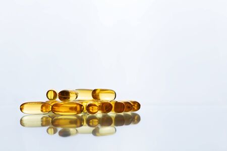 A pile of yellow Amega capsules lying on a light gray background. Front view with a copy space....