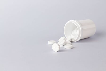 White pills spilling out of pill bottle on gray table. Front view with copy space. Medicine concept. Medicines.の写真素材