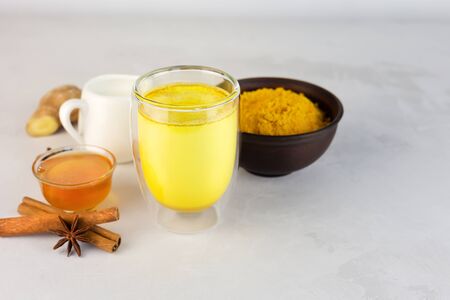 Golden milk and ingredients for preparation: turmeric, honey, ginger root, cinnamon, badian on a gray. The concept of alternative medicine. Masala Haldi Doodh.の写真素材