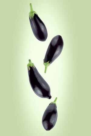 Falling eggplants isolated on a green background with clipping path as package design element and advertising. Flying vegetables.の写真素材