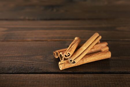 A pile of cinnamon sticks lies on a brown wooden table. Front view, copy space.の写真素材