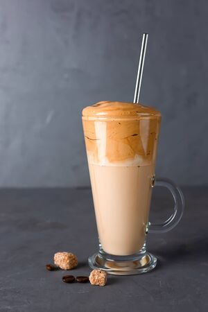 Iced Dalgona coffee in tall glass on a grey background. Trendy korean fluffy creamy whipped coffee. Vertical photo.の写真素材