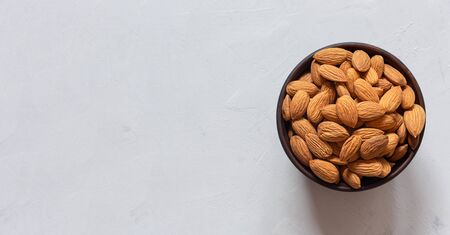 Almonds in a brown clay bowl on a gray background with a copy space. Banner. Top view.の写真素材