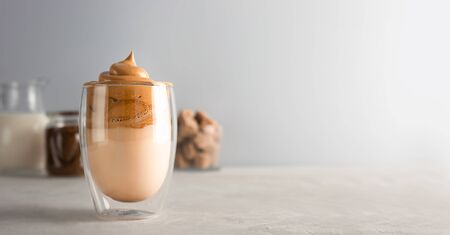 Trend korean drink with foam. Glass with Dalgona frothy coffee on grey table. Banner with copy space.の写真素材