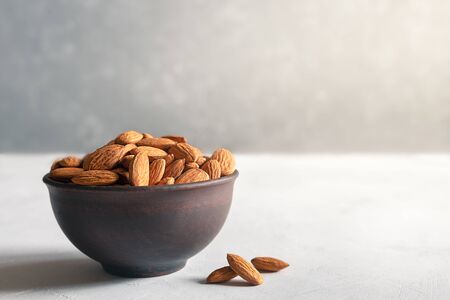 Almonds in a brown clay bowl on a gray background with a copy space.の写真素材