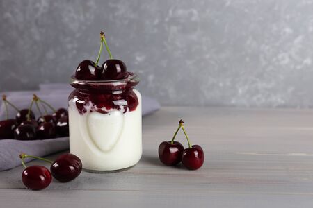 Dessert made of natural yoghurt, jam and cherries on a grey wooden background. Healthy food. A portion of dessert in a glass. Copy space.の写真素材