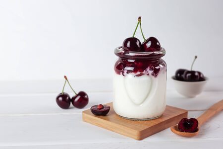 Natural yoghurt, jam and cherries on a white wooden background. Healthy food. A portion of dessert in a glass. Copy space.の写真素材