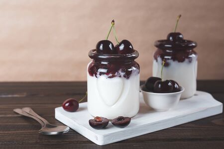 Natural yoghurt, jam and cherries on a brown wooden background. Healthy food. Dessert. Copy space.の写真素材