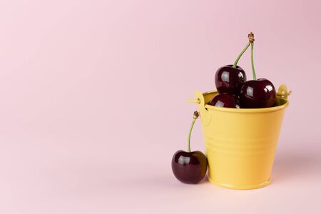 Fresh, ripe cherries in a small yellow bucket on a pink background with a copy space.の写真素材
