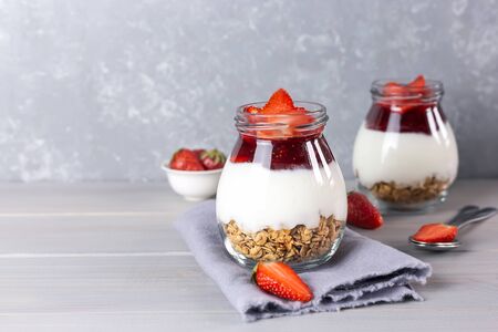 Jars of granola with yogurt, strawberry jam and fresh strawberries on a gray wooden background. Healthy vegan breakfast concept.の写真素材